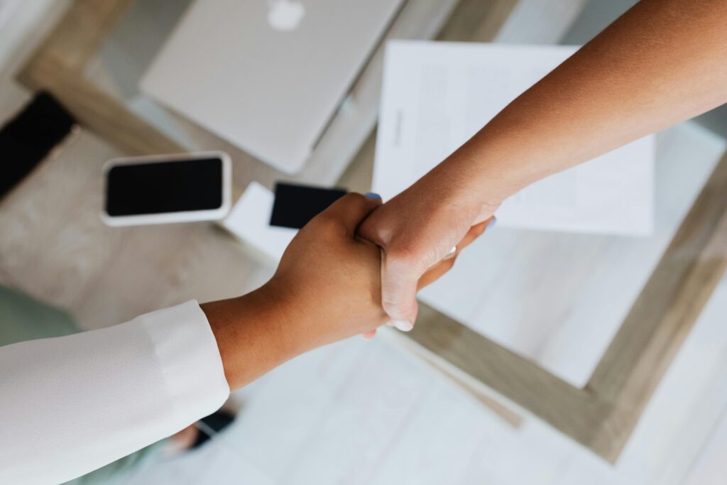 pexels-photo-5398881-5398881 Two people shaking hands over a desk with modern tech, symbolizing a successful business agreement.